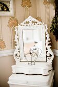 Dressing mirror with carved frame painted white on small table in corner