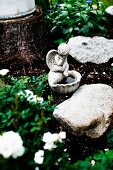 Bird bath with small cherub figurine amongst boulders in flowerbed