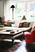 Gemütliche Loungeecke, roter Polstersessel und weisses Sofa um Holztisch, auf poliertem Terracottaboden