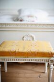 Antique, Regency-style stool painted white with gold, patterned cover at foot of bed