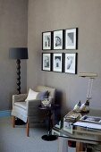Corner of desk, armchair and standard lamp with black lampshade next to photos on brown-painted wall