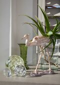 Ornamental glass spheres and long-legged bird ornament in front of aloe leaves in vase