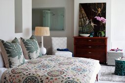 Double bed with country-house-style patterned bedspread and leaf-patterned scatter cushions in bedroom with ensuite bathroom