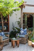 Korbstühle mit Batikkissen und afrikanischer Beistelltisch auf Terrasse mit Pflanztöpfen