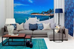 Set of coffee tables and grey sofa in front of mural wallpaper showing azure sky above tropical island