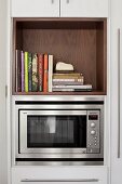 Küchenschrank mit Mikrowelle, darüber Kochbücher in Regalöffnung aus Holz