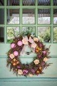 An Tür aufgehängter Kranz mit Blüten und Weihnachtskugeln