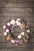 Wreath decorated with flowers and baubles on wooden surface