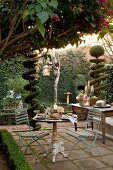 Festively set bistro table on terrace and buffet on table between topiary bushes in garden
