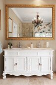 Gilt-framed mirror above white, antique cabinet with built-in twin sinks