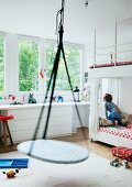 Child's bedroom with swing suspended from ceiling; child sitting on bunk beds and large window with garden view