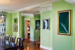 Cropped wooden dining table and chairs and paintings mounted on green walls; West Palm Beach; USA