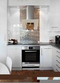Moderne weiße Einbauküche mit Edelstahl Dunstabzug und Spritzschutz mit reflektierenden Mosaikfliesen
