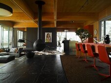Black slate floor in contemporary wooden house with suspended fireplace and red swivel chairs in dining area to one side