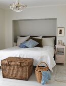 Wicker trunk at foot of double bed with headboard in niche in white bedroom