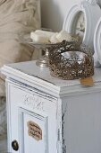 Vintage, hand-crafted metal wreath next to soap in silver-coloured bowl on shabby-chic bedside cabinet