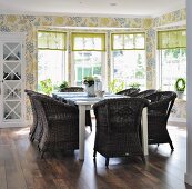 Comfortable dining set with wicker armchairs in front of bay windows and floral wallpaper