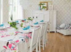 Table festively set with floral tablecloth in white dining room