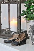 Worn child's shoes used as ornaments in front of antique lantern and potted ivy