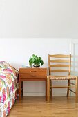 Bedside table, pale wooden chair and bed with bright bedspread in attic room