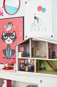 Colourful children's posters on wall and doll's house on cabinet