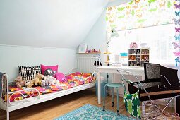 Colourful bed linen and soft toys on metal bed, retro doll's pram and desk below window