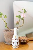 Still-life arrangement in retro jug-style vase, delicate geranium in clay pot and jewellery box