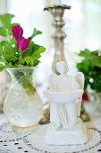 White china angel figurine next to glass vase of purple flowers