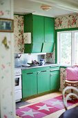 Kitchen cabinets with green doors and rug with star motif on wooden floor