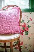 Pink floral cushion on Thonet chair against wall with floral wallpaper