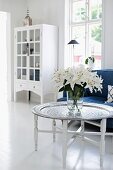 Vase on white lilies on tray table and blue sofa with white, glass-fronted cabinet in background