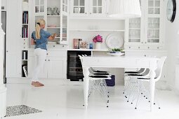 White dining table and classic Eames chairs in front of white dresser in rustic dining room; woman in background