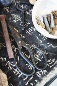 Traditionelle Bonsaischere und kleine Objekte auf einer Steinplatte mit eingeritzten, japanischen Schriftzeichen