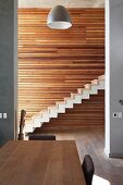 Essplatz vor raumhohen Durchgang und Blick auf minimalistische Treppe mit Holzstufen auf Betonfertigtreppe, an Wand horizontale Holzverkleidung