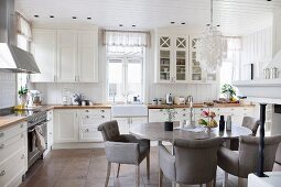 Gemütlicher Essplatz mit grauen Polsterstühlen um ovalen Esstisch in weisser Landhausküche