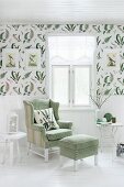 Reading chair with matching footstool below window; white wainscoting below decorative wallpaper with pattern of fern