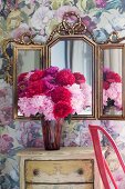 Peonies on vintage chest of drawers below ornate vanity mirror on wall with romantic floral wallpaper