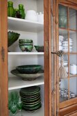 Glass-fronted cabinet with open door and view of green ceramic crockery