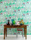 Green floral wallpaper, table and colourful glass vases