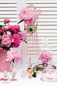 Romantic, pretty arrangement of peonies & wire necklace rack shaped like tailors' dummy on table