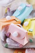 Colourful, spring-themes paper gift boxes shaped like handbags with handles and pompoms