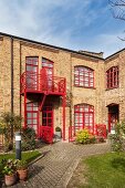 Former factory converted into residential building; red-painted window frames and balcony rails, courtyard with edged flowerbeds and paved paths