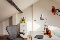 Home Office auf Galerie - Grauer Bürostuhl vor Schreibtisch mit Tischleuchte, im Hintergrund Büroschrank