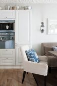 Gemütlicher Essplatz mit schlichten Polstermöbeln und floralen Kissen in Wohnküche; Spiegelung auf Backofen in Einbauschrank