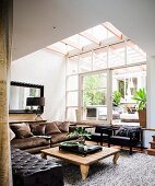 Rustic wooden coffee table, grey-brown velvet sofa and black armchairs under large skylight