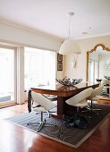 White swivel chairs and solid-wood table under white pendant lamp in front of mirror with curved gilt frame in minimalist traditional interior