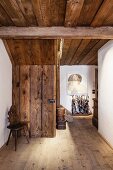 Antique plank chair in rustic hallway of restored farmhouse; contemporary painting above traditional umbrella stand in background