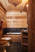 Wooden walls, ceiling and furnishings combined with black slate tiles in rustic, modern bathroom