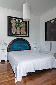 French bed with antique, semicircular headboard below picture on wall; pedant lamp with white, cylindrical fabric lampshade in foreground