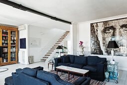 Black sofa set in open-plan interior with large photo portrait and staircase in background